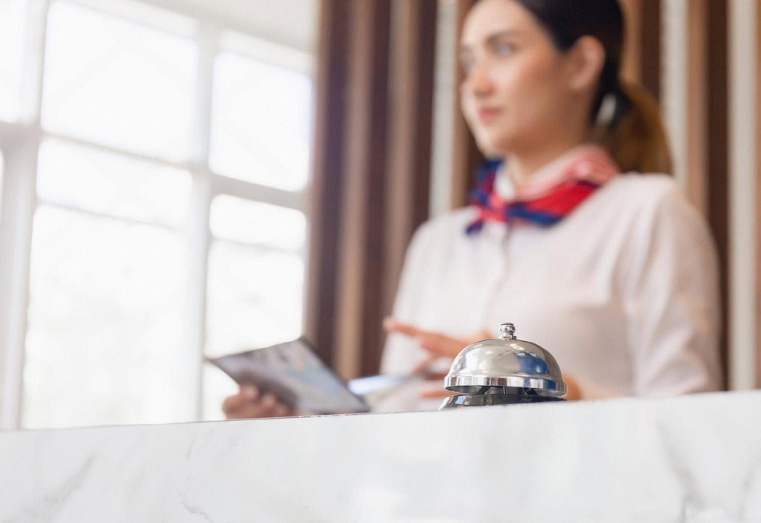 Hotel receptionist standing behind a marble desk with a silver service bell, illustrating traditional front-desk communication