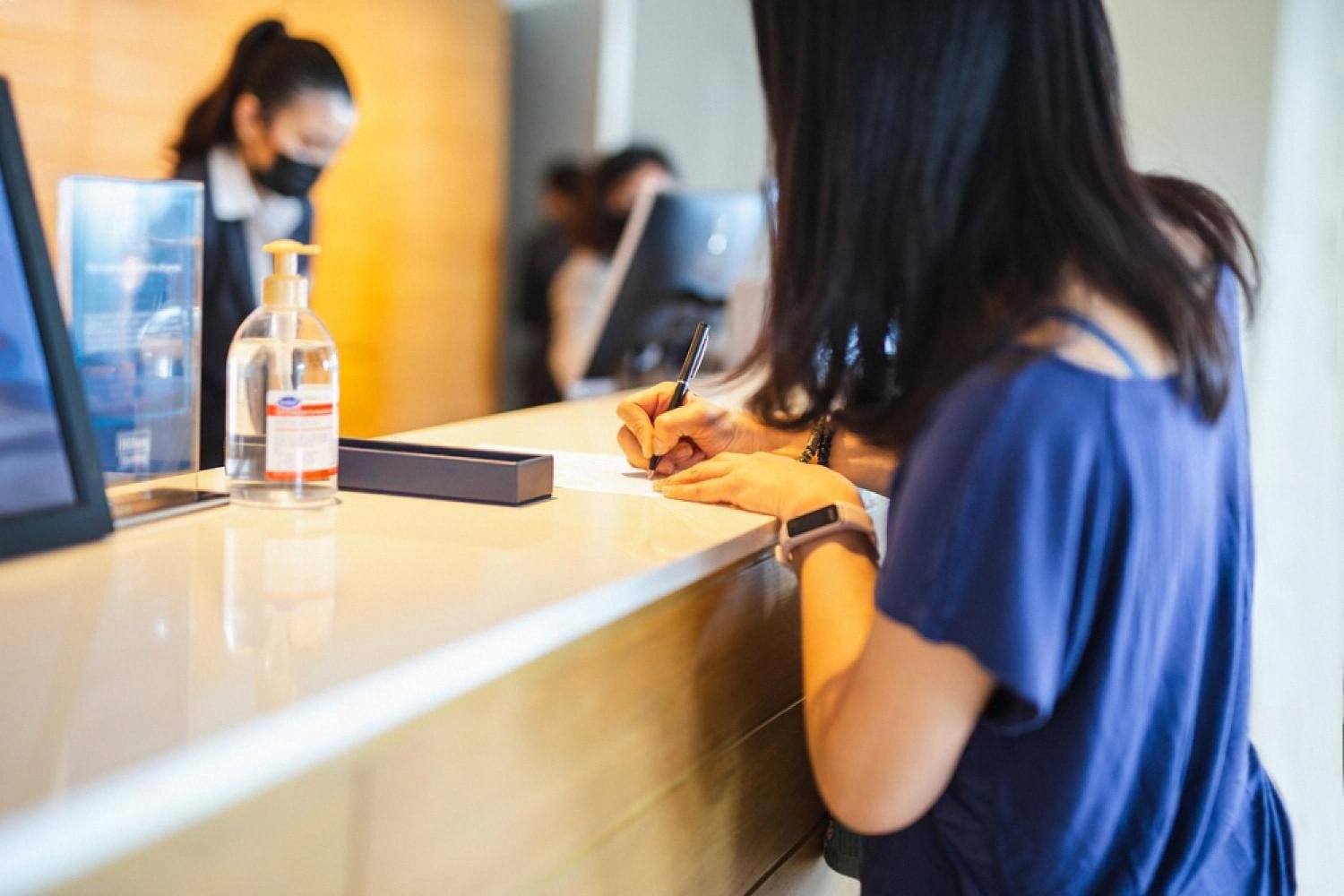 A guest signing paperwork at a reception counter while a staff member assists, showing face-to-face communication